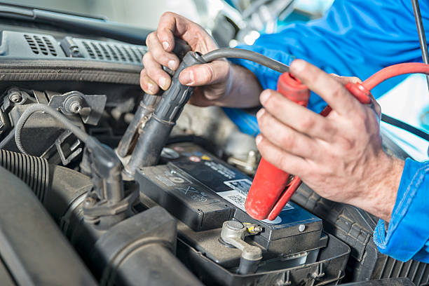 A car mechanic uses battery jumper cables to charge a dead battery.